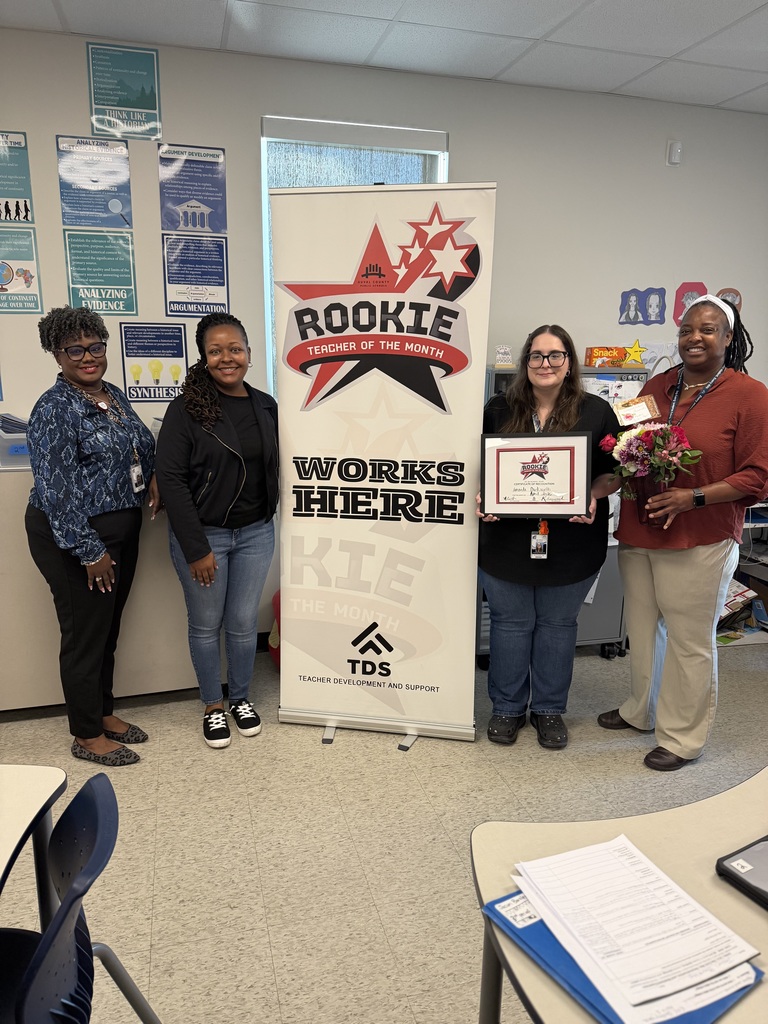 Amanda Duckworth stands next to a colleague holding her Rookie Teacher of the Month certificate in a classroom.