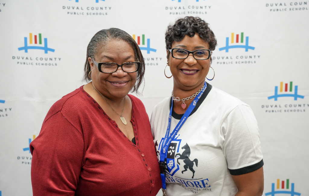 Two women posing in front of a Duval County Public Schools backdrop