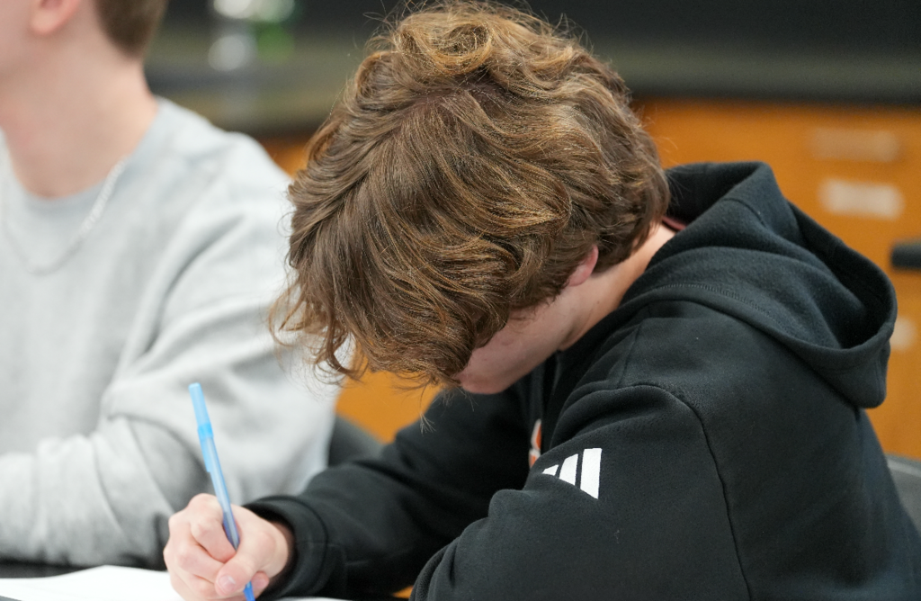 Student writes notes in a notebook during a classroom lesson.