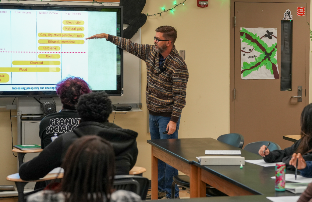 Dr. Scott Sowell, an older teacher, leans over to help a student with a classroom assignment.