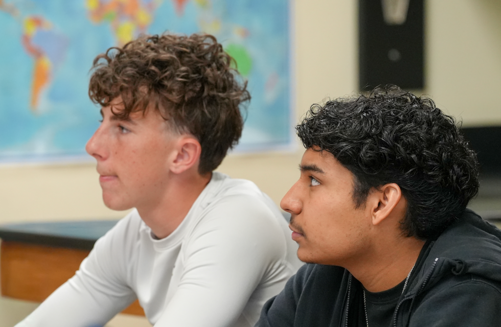 Student listens attentively during class discussion while seated at a desk.