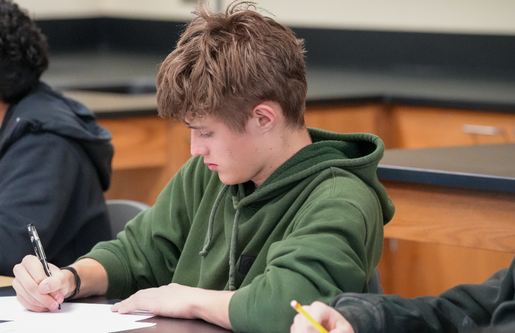 Student writes notes in a notebook during a classroom lesson.