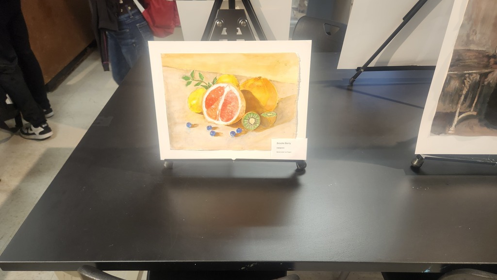 A framed painting of fruit, including a grapefruit, lemon, and blueberries, displayed on a black table.