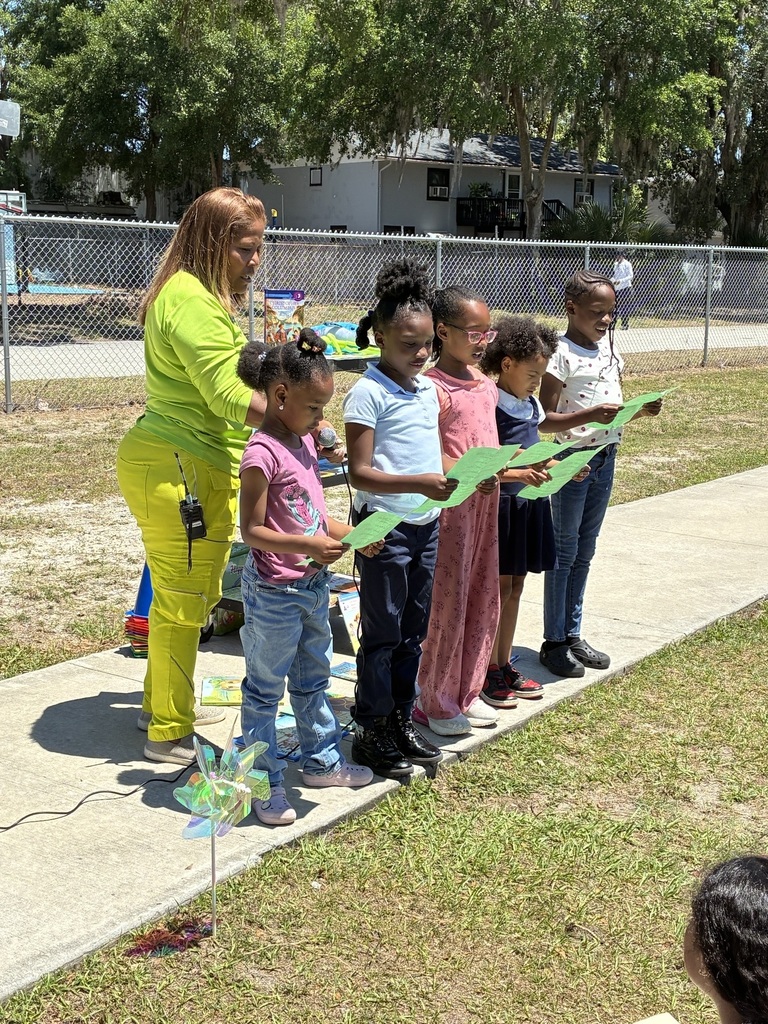 A woman and children stand on a sidewalk, holding green paper