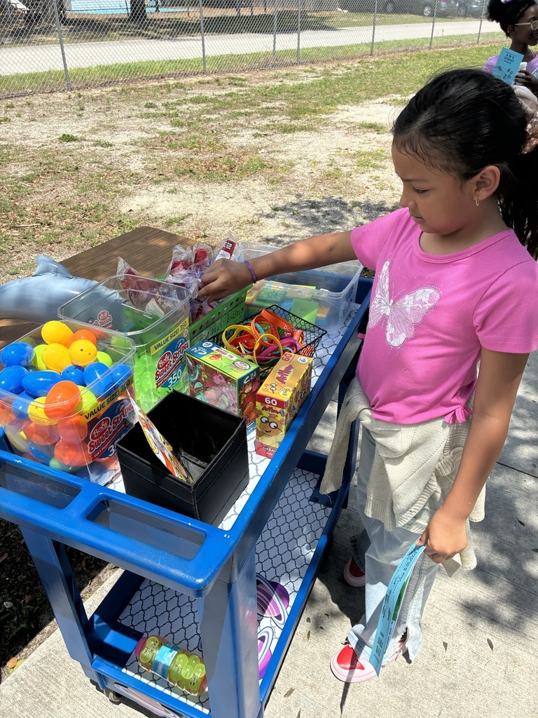 A child in a pink shirt and white skirt chooses toys from a cart with colorful items.