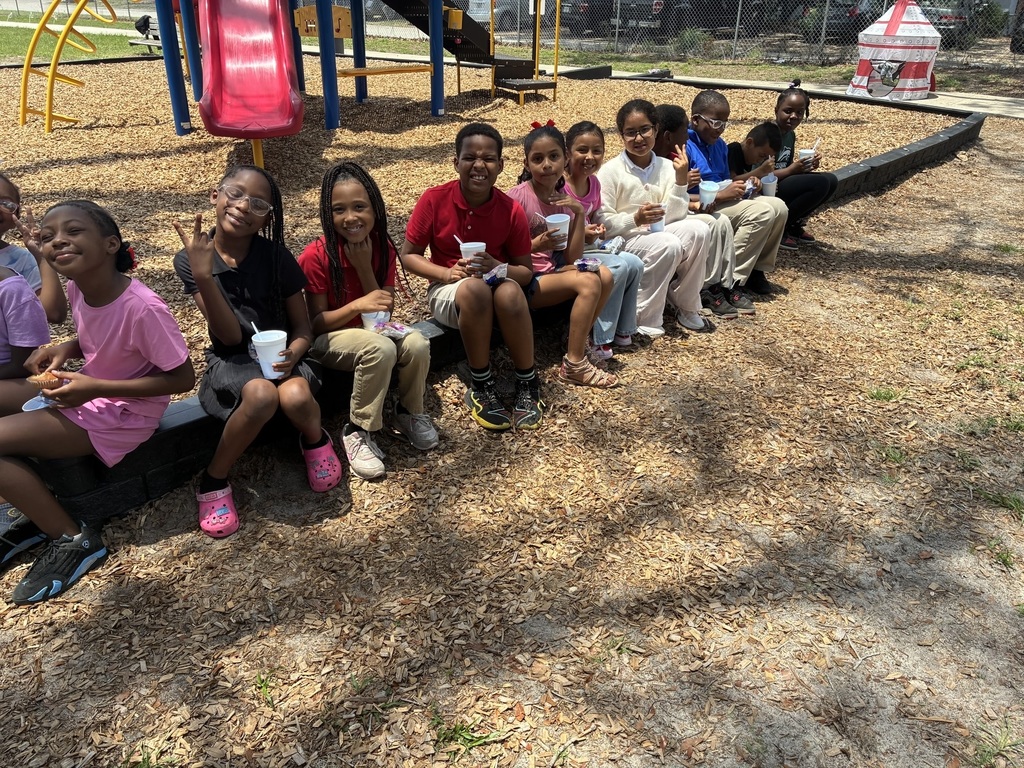 Children sit on a bench in a playground with cups, some holding up a peace sign.