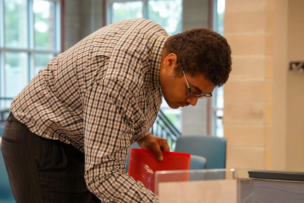 A person leans over a red object in a glass case, inside a modern building.