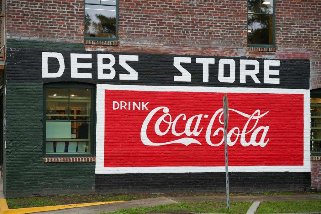 A building with a brick facade displays a large Coca-Cola advertisement. The sign reads "Drink Coca-Cola" in white letters.