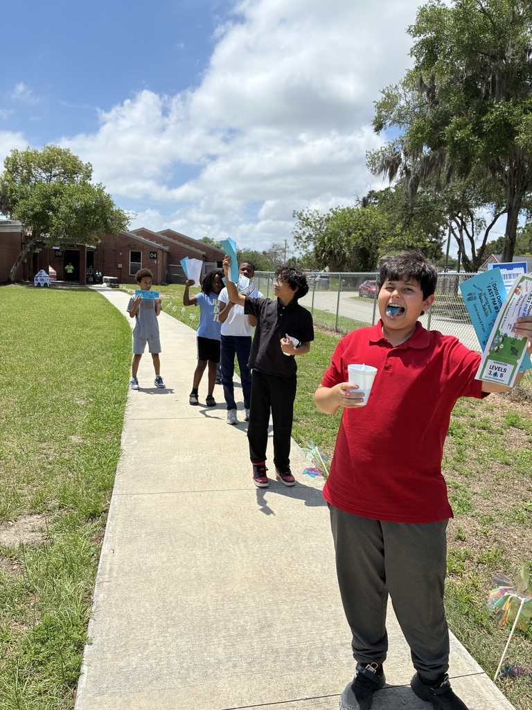 A group of students on a sidewalk; Buildings, trees, and grass in background.