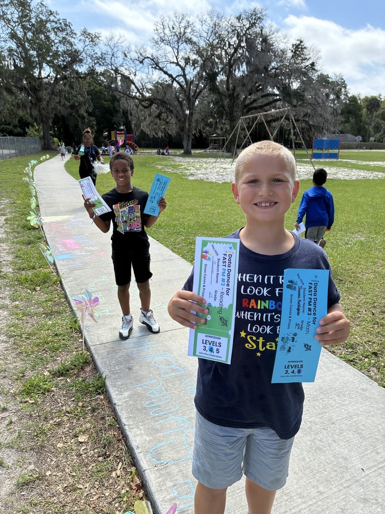 Children along a sidewalk holding up a blue ticket while another child follows behind. 