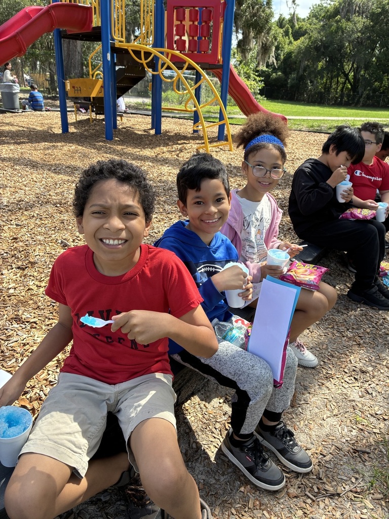 children are seated on a bench at a playground with snowcones