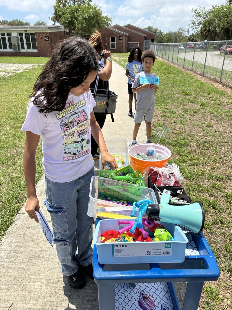 A young girl with long hair stands by a table with various items, looking at a blue box.