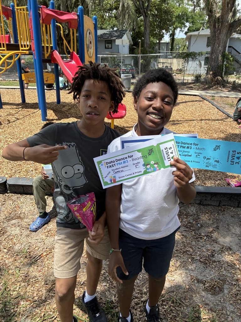 Two children standing in front of a playground, one holding a certificate