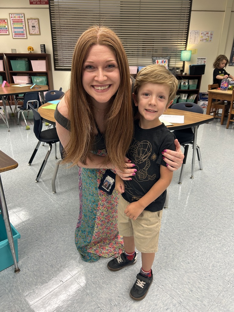 A teacher smiles while posing with a student in her classroom