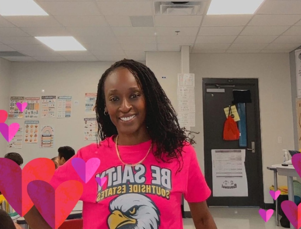 A teacher stands smiling in her classroom