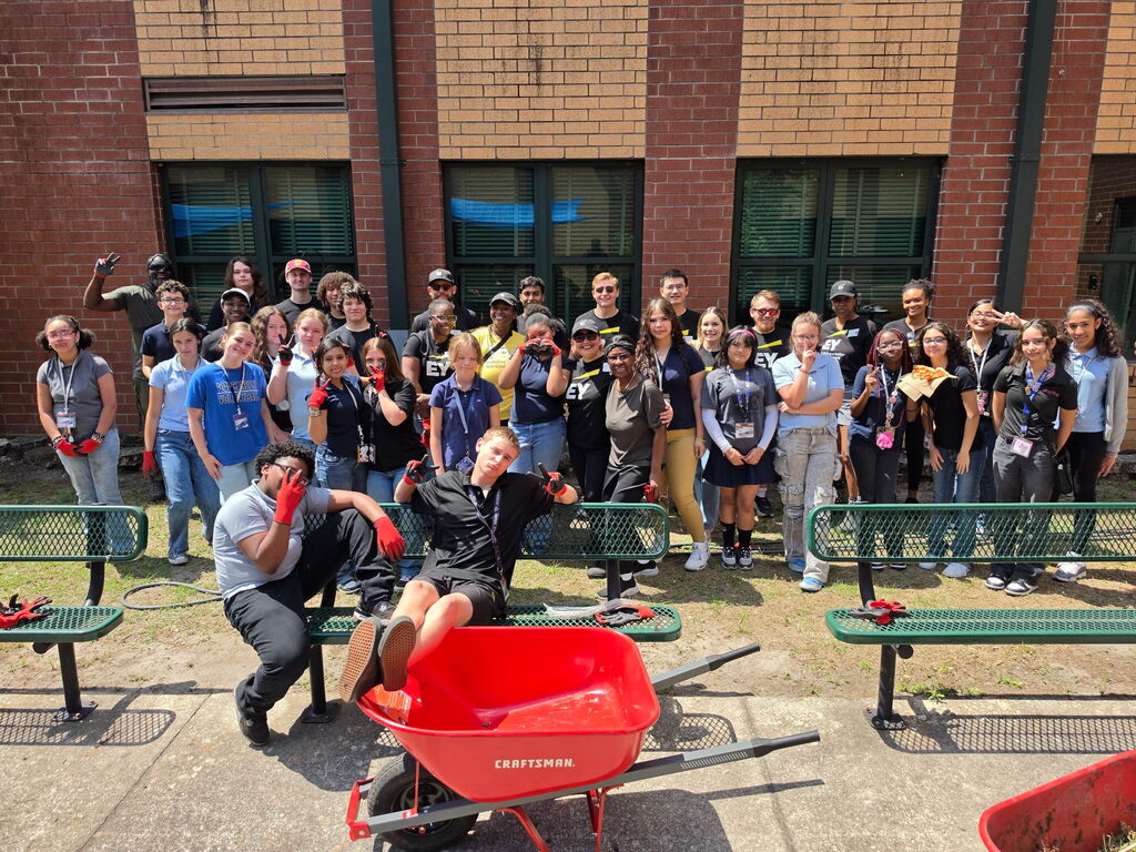 A group of student volunteers stands smiling with Ernst and Young volunteers in a newly refurbished school courtyard. 