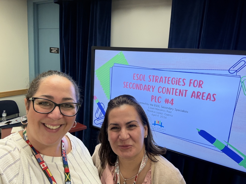 Two teachers pose at a professional learning program, in front of a screen which reads "ESOL strategies for secondary content areas". 