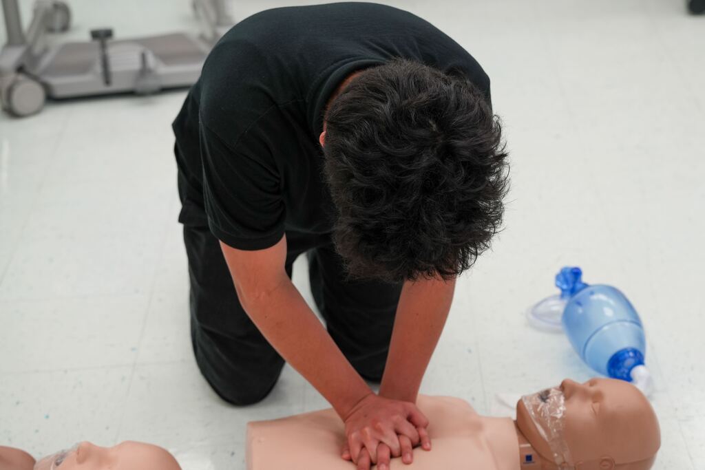 A person kneels over a CPR manikin on the floor, practicing chest compressions with both hands.
