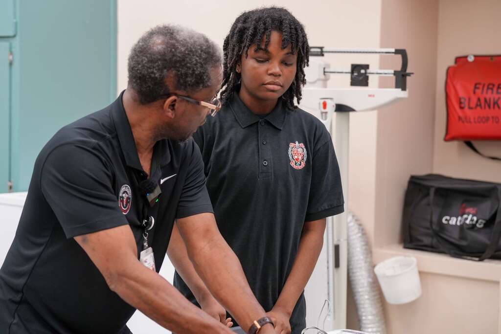 A man and woman in black uniforms are practicing first aid, standing near a fire extinguisher and medical equipment.