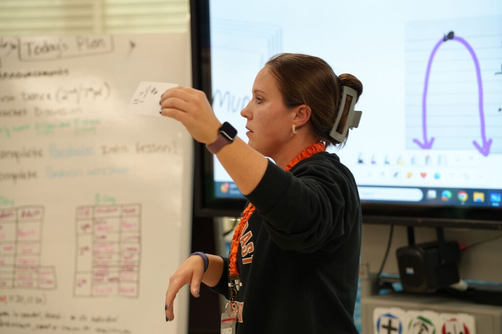 Woman teaching with a whiteboard, a large screen projector, and a computer monitor displaying a graph.