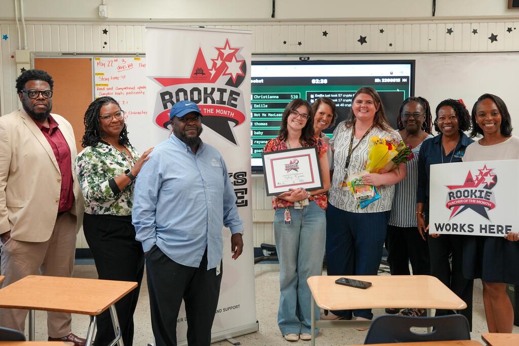 A group of eight people in a classroom, with some holding awards and signs.