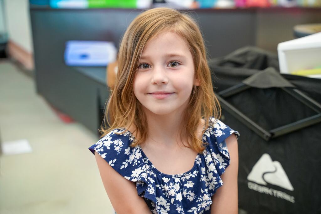 A young girl with blonde hair smiles and poses for a picture in a room with a black countertop and storage bags.
