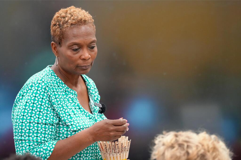 A woman in a green blouse holds a bunch of incense sticks in an outdoor setting.