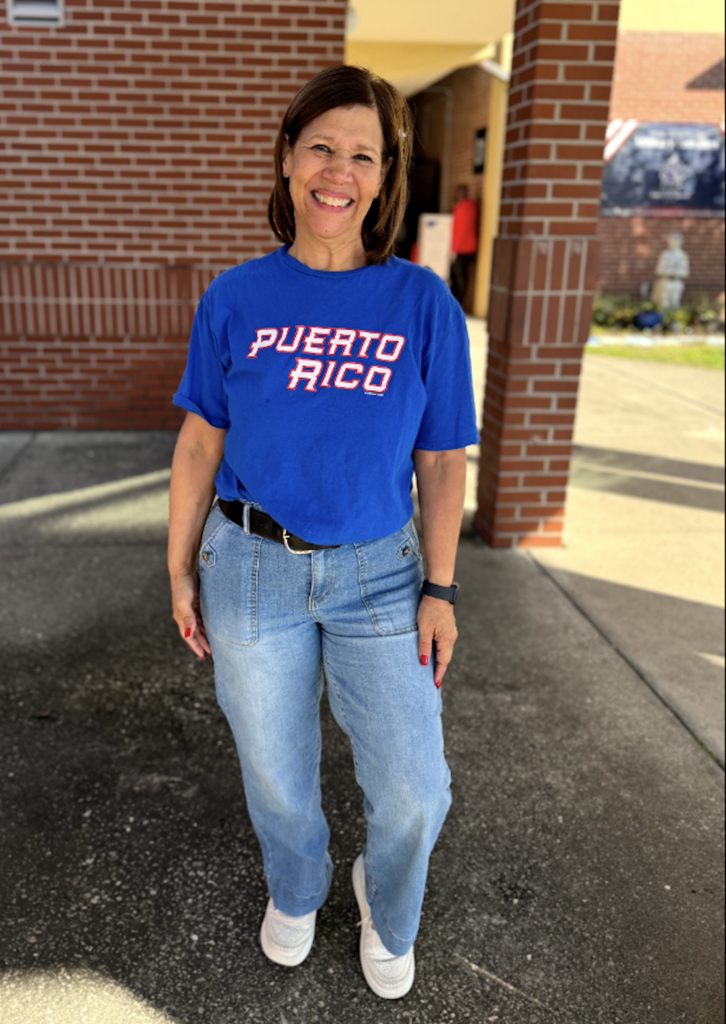 Mrs. Cosme stands smiling for a photo in the school courtyard. 