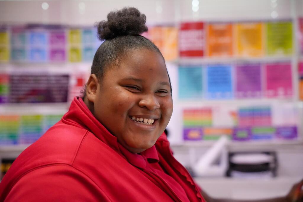 A person with a bun hairstyle smiles for a picture in a room with shelves of colorful papers.
