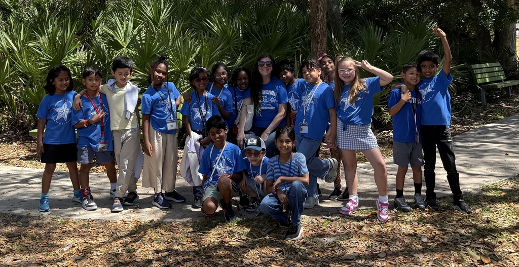 A group of studnets stands smiling around a teacher at the Jacksonville Zoo.