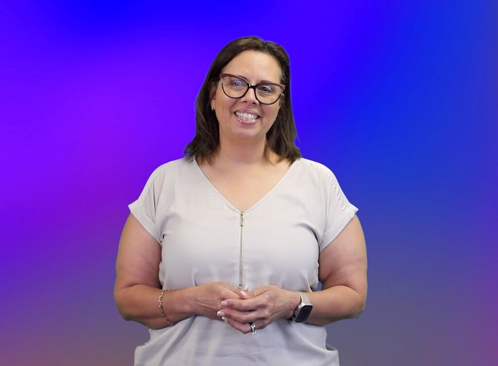 Adele Herring stands smiling for a photo taken in front of a plain blue background.