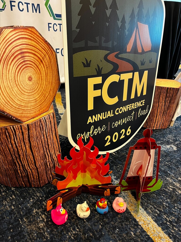 Logs, a sign reading "FCTM Annual Conference 2026", and a fire pit display on a table with a yellow line.