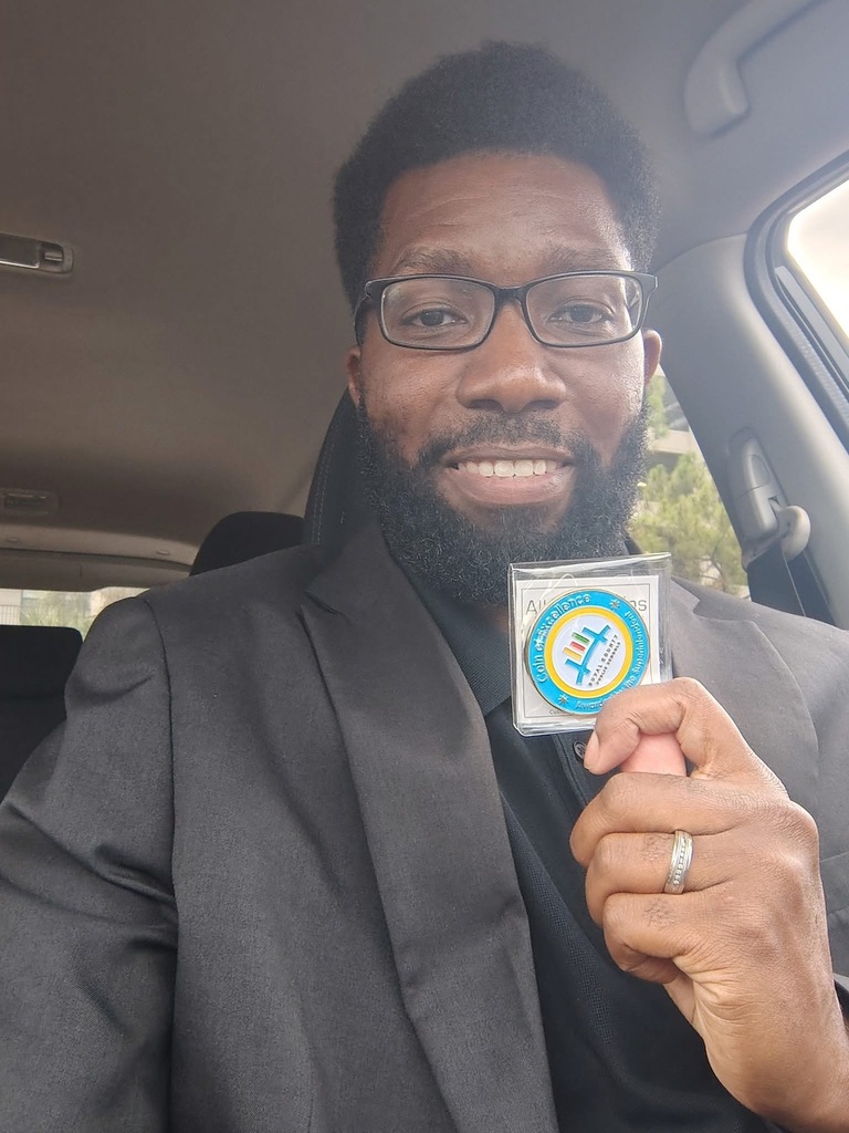 Assistant Principal Jeremy Greene smiles while holding a Duval County Schools Coin of Excellence award.