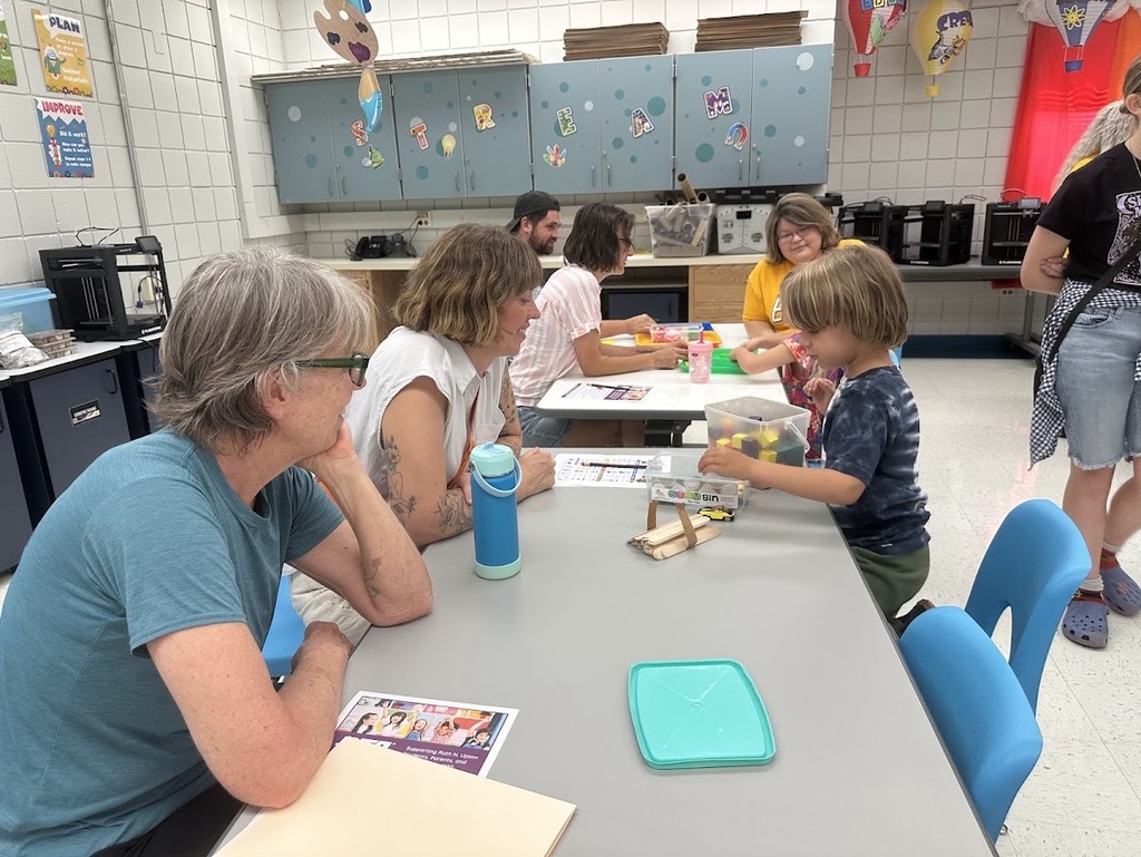 Two adults at a table with a child, working on an activity together