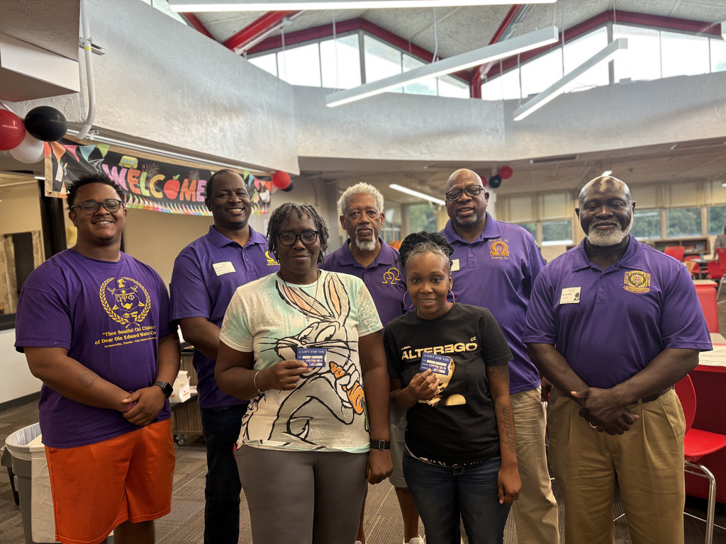 Several people in matching purple shirts stand in a room, smiling for a photo. A woman holds a book.