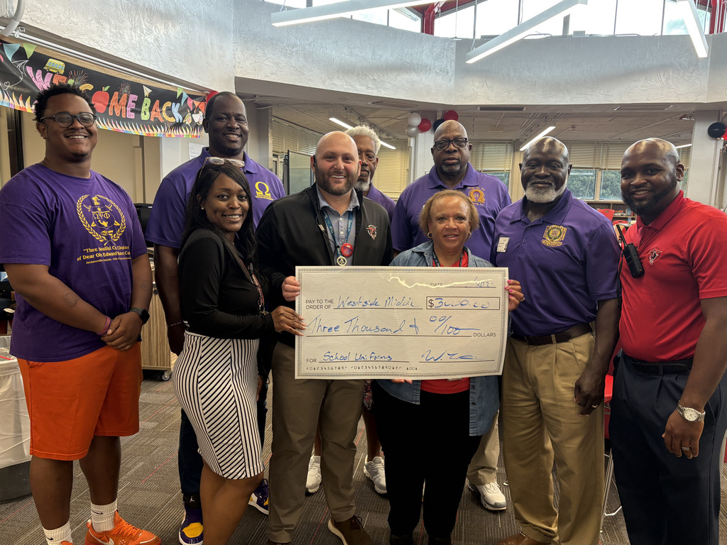 Group of people in matching purple shirts pose with a check, standing in a library.