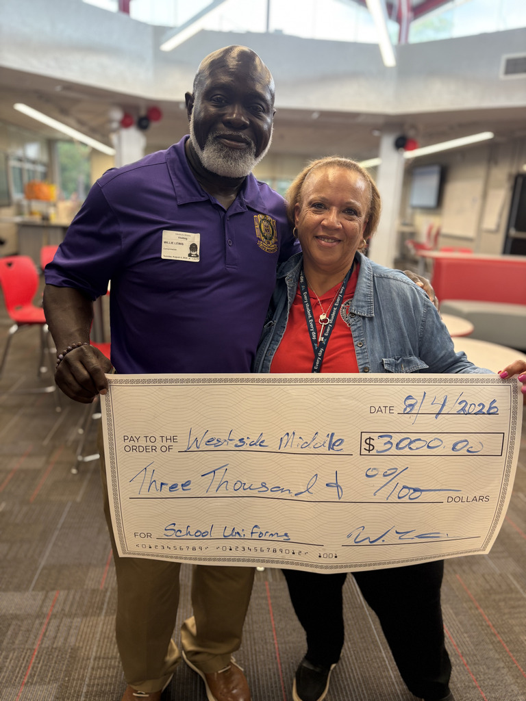 Two people hold a check for $3,000. The person in the purple shirt holds the check by the left side.