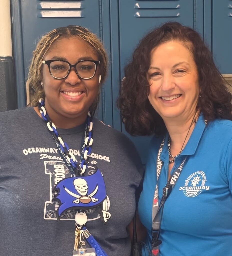 Two smiling women standing together in front of blue school lockers — School Counselor Jasmine Young on the left in an Oceanway Middle gray Buccaneers shirt and Ms. Stansel on the right in a blue Oceanway polo.