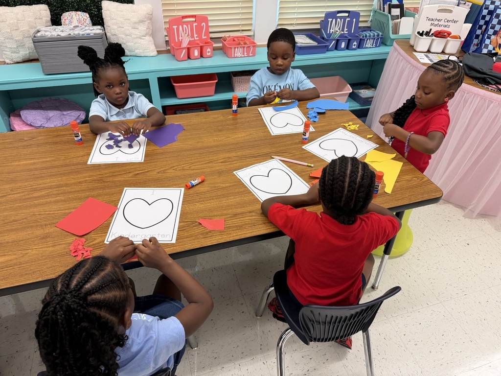 Five children sitting around a table with crafts. Each child is working on a heart-shaped paper.