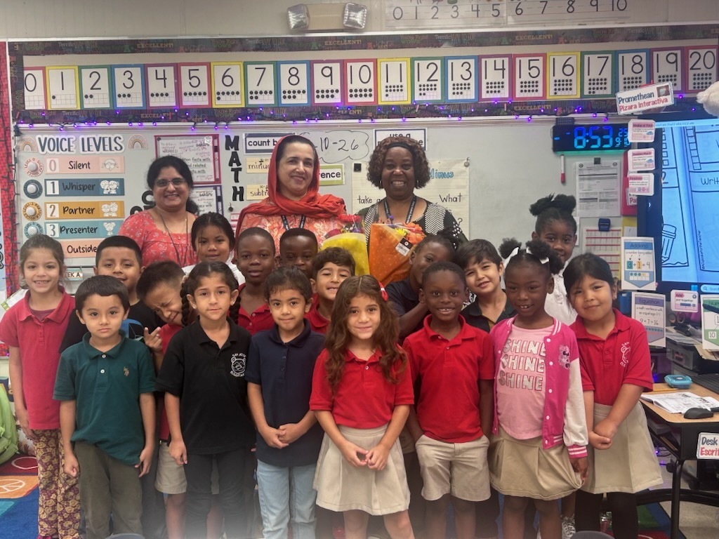 A group of students in school uniforms pose in a classroom with a teacher.