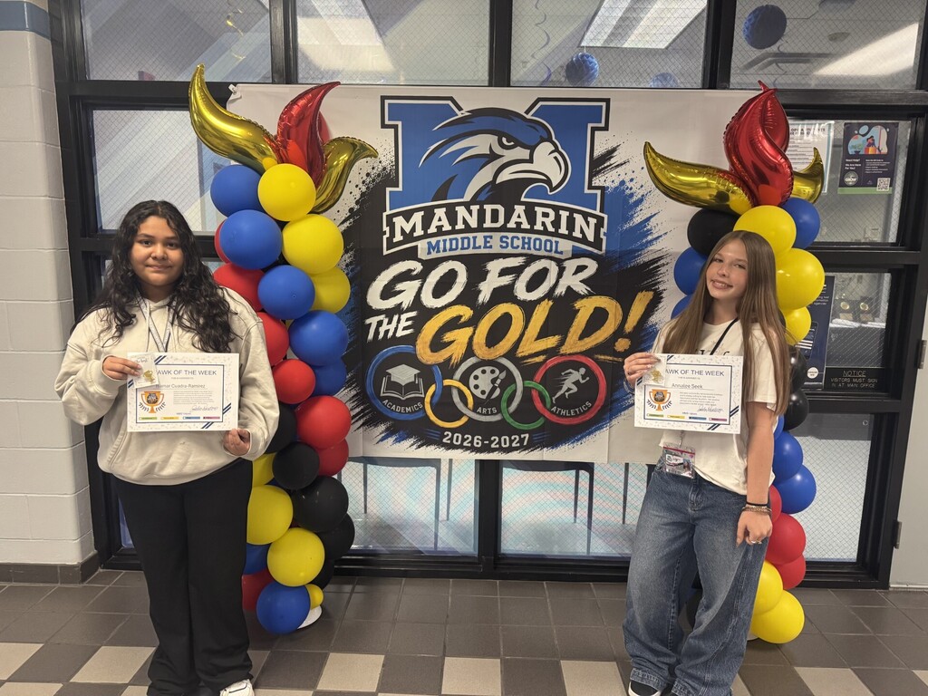 Two students stand, holding certificates, in front of a "Go for the Gold" banner with balloons.