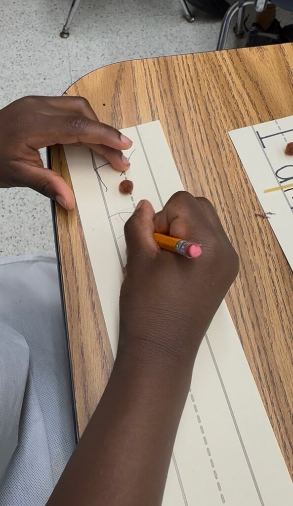 student writing a sentence using spaghetti noodle and pom pom "meatball" as spacers