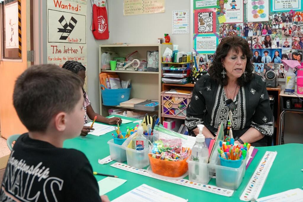 Teacher and student seated at a table, engaged in an activity, surrounded by art supplies and papers.