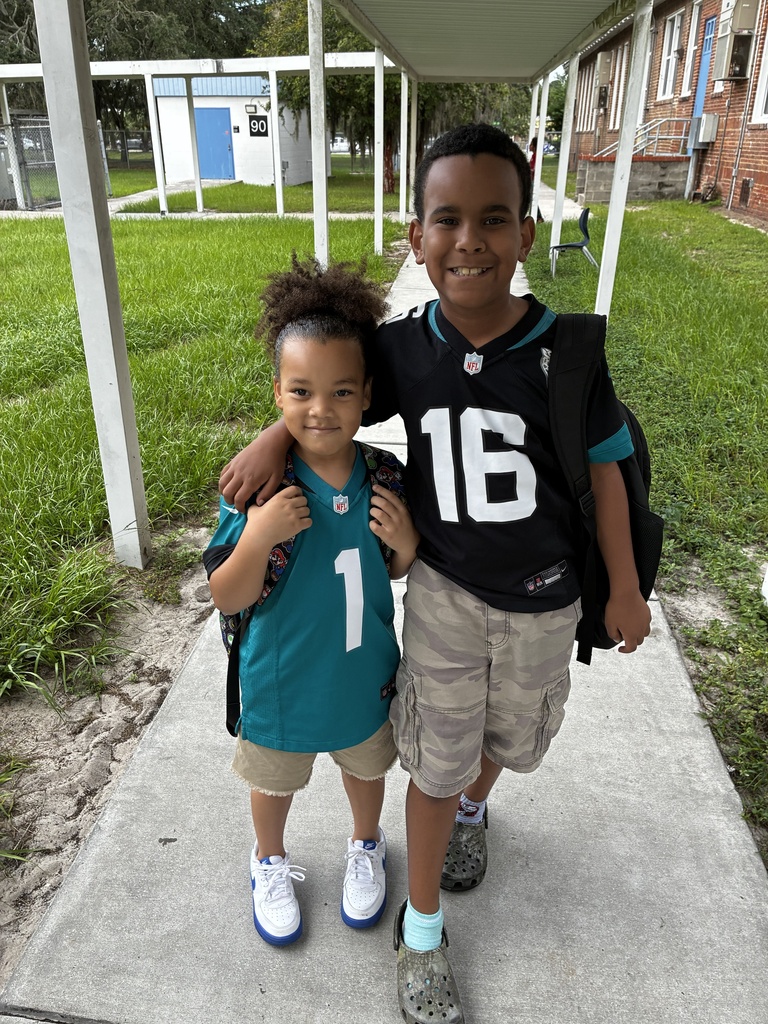 Two children, one in a blue shirt and the other in a black shirt, stand together on a concrete path.