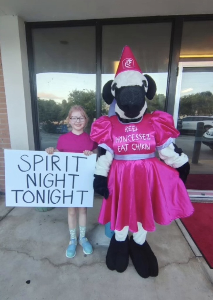 A young girl and the Chick-Fil-A mascot in a pink costume holding a sign that says "Spirit Night Tonight."