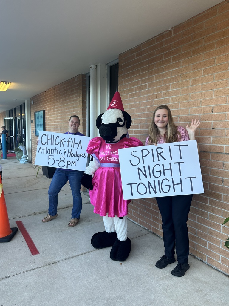 Three individuals stand in front of a brick wall. One holds a sign reading "Chick-fil-A Atlanta Holidays 5-8pm". Another holds a sign that says "SPIRIT NIGHT TONIGHT".
