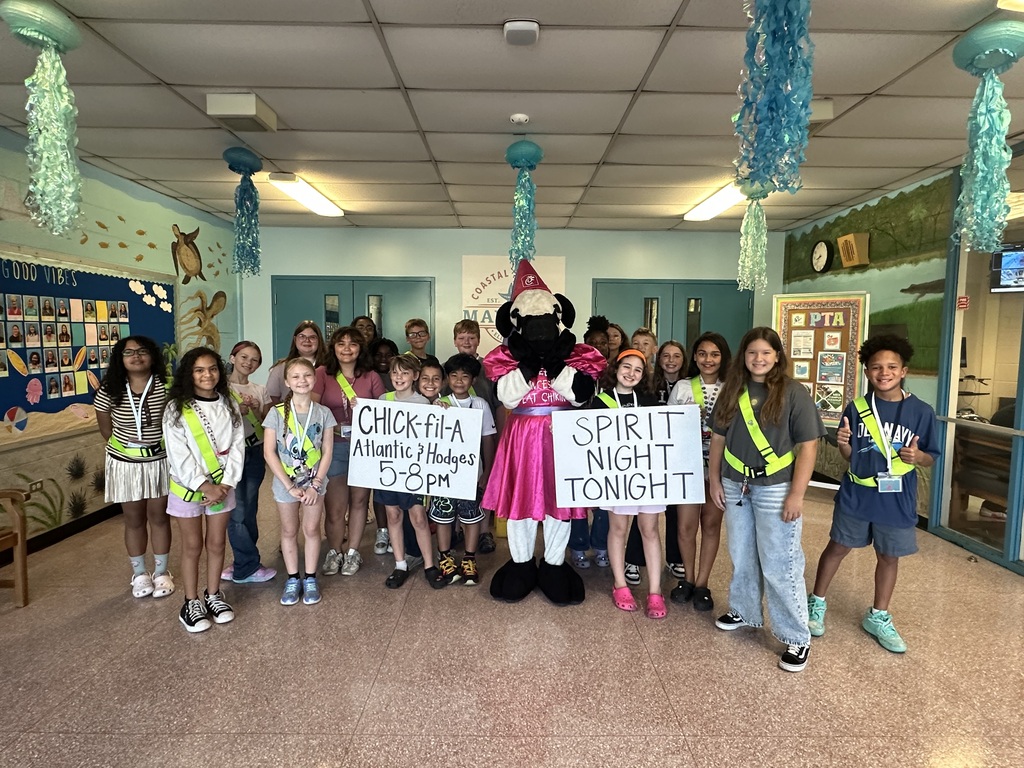 Group of children holding signs, including one with a mascot, in a decorated room.