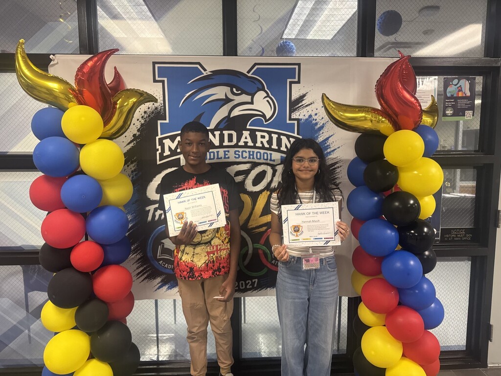 Two individuals stand under balloon arches, each holding certificates. They are in front of a banner with a school logo.