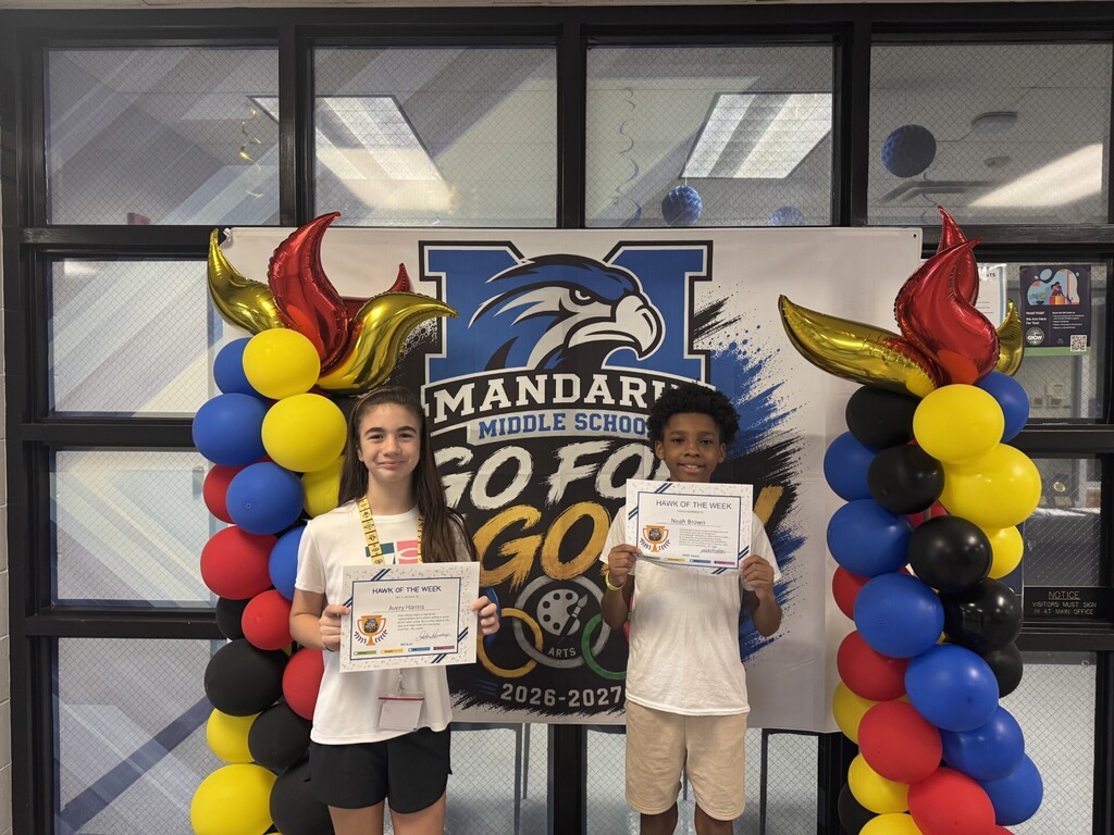 Two students stand with certificates in front of a banner with balloons and a school logo.