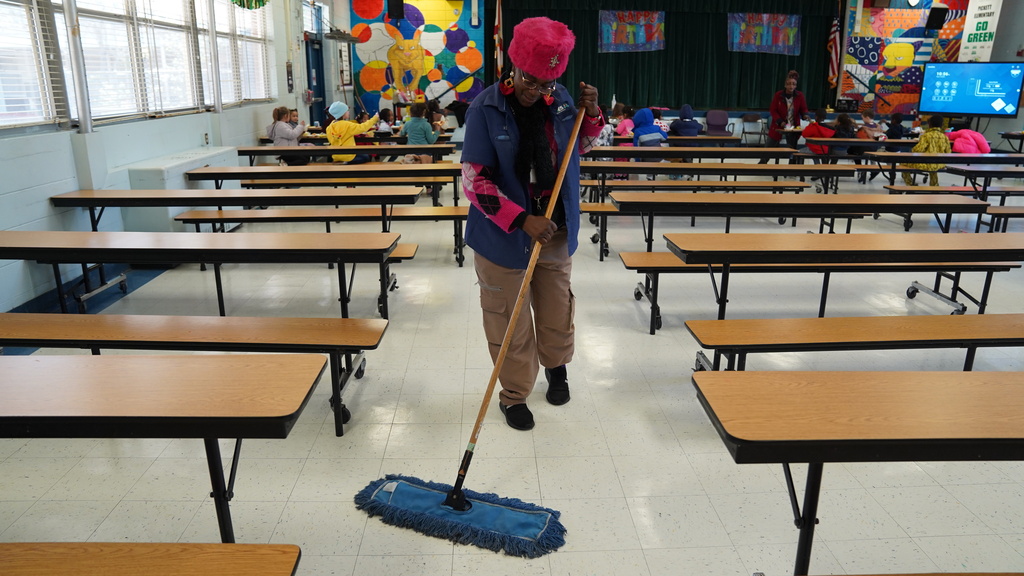 Pickett Elementary head custodian Francine Muller cleaning the cafeteria floor with a blue dust mop.